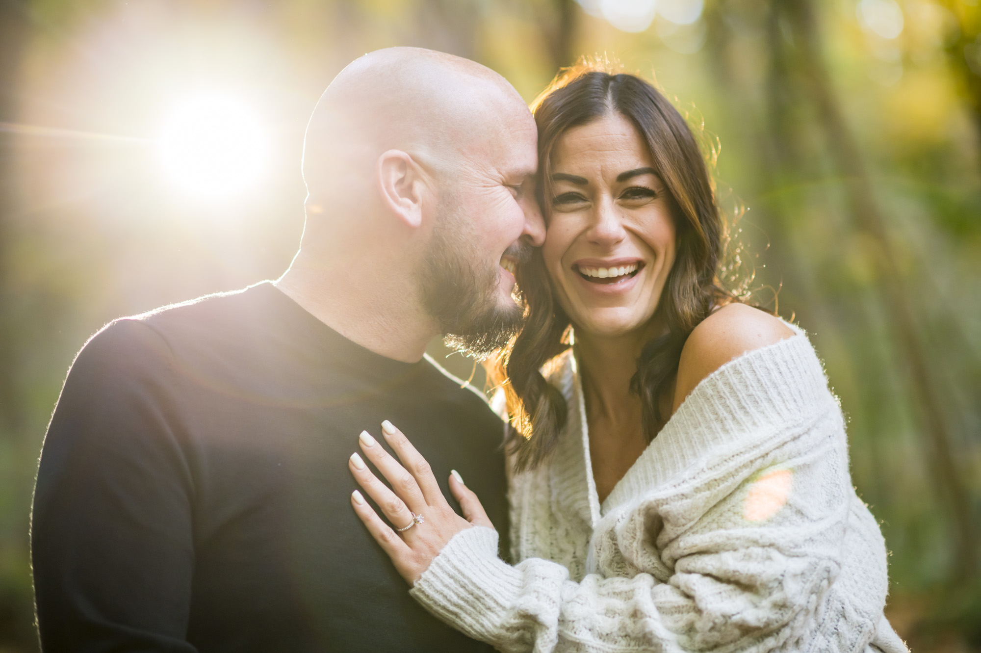 A woman laughs into he camera while her fiance nuzzles her cheek.